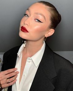 a woman with red lipstick and black blazer holding her hand on her chest, looking off to the side