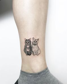 two cats tattoo on the ankle with one cat looking at the camera while the other is sitting down