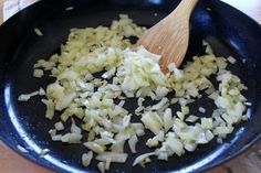 onions being cooked in a skillet with a wooden spoon