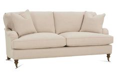 a white couch with pillows on it and some wooden legs in front of the couch