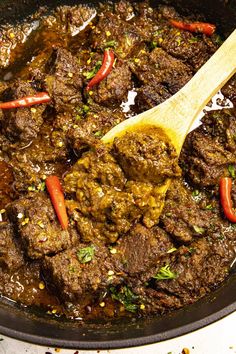 a wooden spoon in a pot filled with meat and peppers on top of a stove