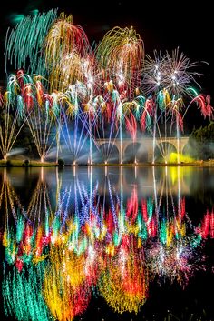 fireworks are lit up in the night sky over water with reflections on the water surface