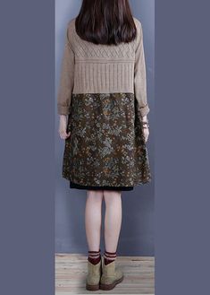 a woman standing in front of a wall wearing a brown sweater and floral print skirt