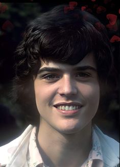 a close up of a person wearing a white shirt and smiling at the camera with hearts in the background