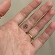 a person's hand with a small sun tattoo on the middle of their finger