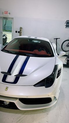 a white sports car with blue stripes parked in a garage next to a bicycle rack