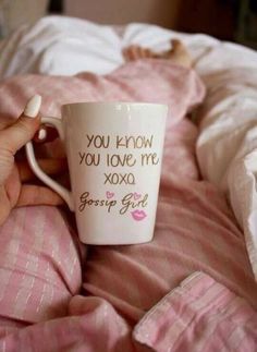 a person is holding a coffee mug in their hand while laying on a bed with pink sheets