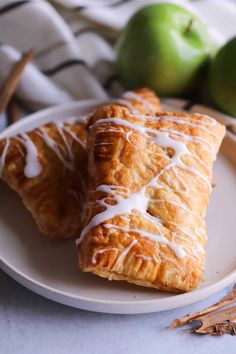 two croissants with icing on a plate next to apples and cinnamon sticks