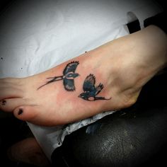 a small tattoo on the foot of a person with two birds flying above them,