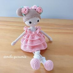 a crocheted doll sitting on top of a wooden table wearing a pink dress