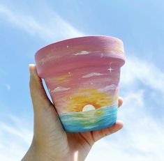 a hand holding up a painted cup in the sky