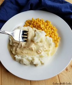 a plate with mashed potatoes, corn and gravy on it next to a fork