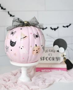 a pink pumpkin decorated with black cats and other halloween related items sits on a white pedestal