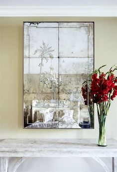 a vase with red flowers is sitting on a table in front of a painting and mirror