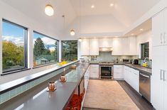 a kitchen with white cabinets and counter tops next to a large window overlooking the trees