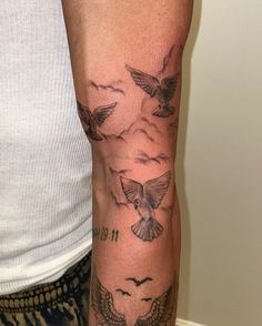 a man with a tattoo on his arm that has birds flying over the clouds and mountains