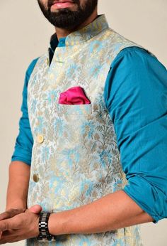 a man with a beard wearing a blue vest and pink pocketed shirt is looking at the camera