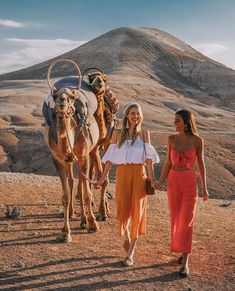 two women are walking with camels in the desert, one is holding her hand