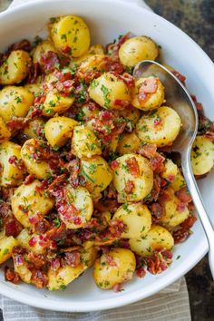 a white bowl filled with potatoes covered in bacon and topped with parsley next to a spoon