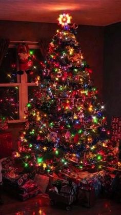 a brightly lit christmas tree in the corner of a room with presents on the floor