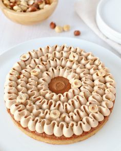 a white plate topped with a cake covered in icing next to a bowl of nuts