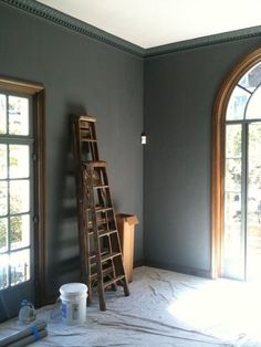 an empty room with a ladder and paint buckets on the floor next to it