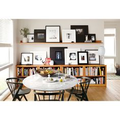 a dining room table and chairs in front of bookshelves with pictures on the wall