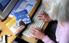 an older woman typing on a computer keyboard with books and other office supplies around her