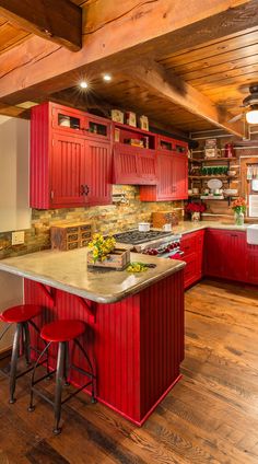 a kitchen with red cabinets and stools next to an island in the middle of the room