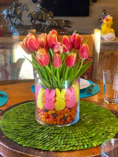 a glass vase filled with candy and flowers on top of a green tablecloth covered place mat