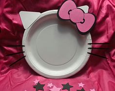 a paper plate with a hello kitty design on the side and stars around it, sitting on a pink satin surface