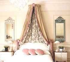 a white bed with pink pillows and canopy over it's headboard in a bedroom