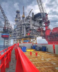 two men are standing on the deck of a boat looking at an oil rig in the ocean