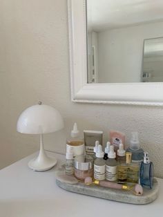 a bathroom vanity with various skin care products and a lamp on the counter top in front of a mirror