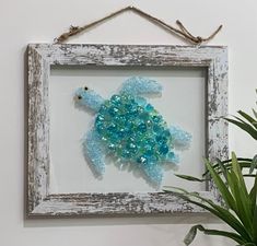 a sea turtle made out of glass beads in a frame next to a potted plant