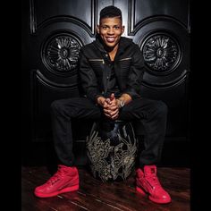 a man sitting on top of a basketball ball in front of a black door with red shoes