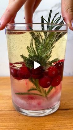 someone is holding their finger over a glass with water and cranberries in it