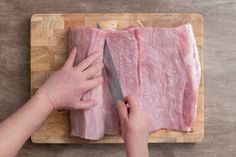 a person cutting up meat on top of a wooden cutting board next to a knife