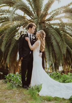 a bride and groom standing in front of palm trees