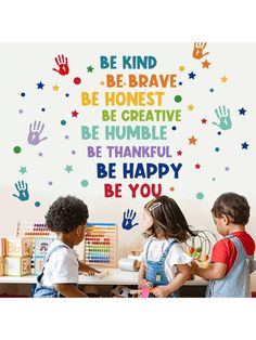 three children are standing in front of a wall with hand prints and words on it