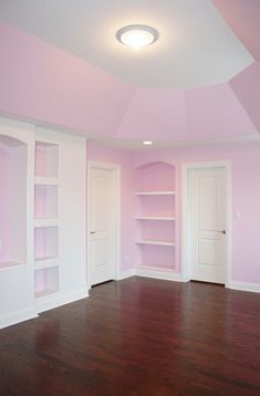 an empty room with pink walls and white bookcases on the far wall, hardwood floors