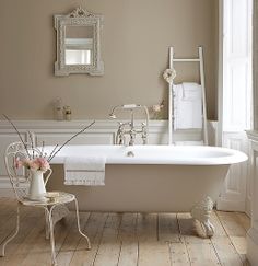 a white bath tub sitting in a bathroom next to a mirror and chair with flowers on it