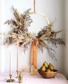 a table topped with a bowl of fruit next to candles and a wreath on the wall