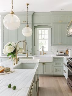 a kitchen with green cabinets and marble counter tops, two pendant lights over the sink