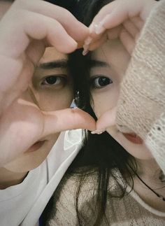 a woman making a heart with her hands while holding something in front of her face