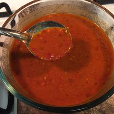 a glass bowl filled with red sauce on top of a stove burner next to a metal spoon