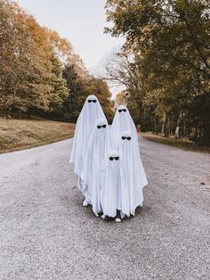 two ghost like figures standing in the middle of an empty road with trees behind them