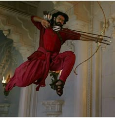 a man dressed in red jumps into the air with his bow and arrow