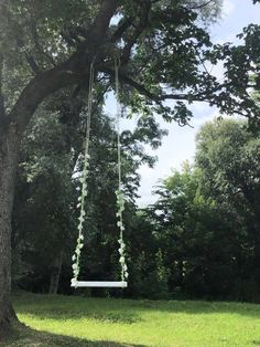 a white swing hanging from a tree in the middle of a grassy area with trees