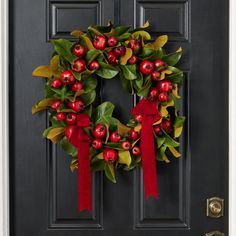 a wreath with red berries and green leaves hangs on the front door's black door